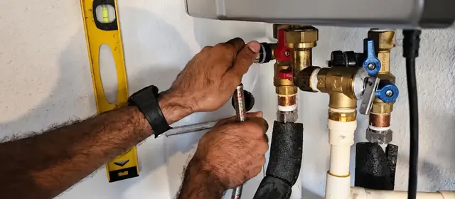 Hands connecting valves on a wall mounted tankless water heater